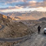 Complete Ladakh travel guide showing a scenic mountain road near Leh with Himalayan landscapes and a traveler exploring Ladakh.